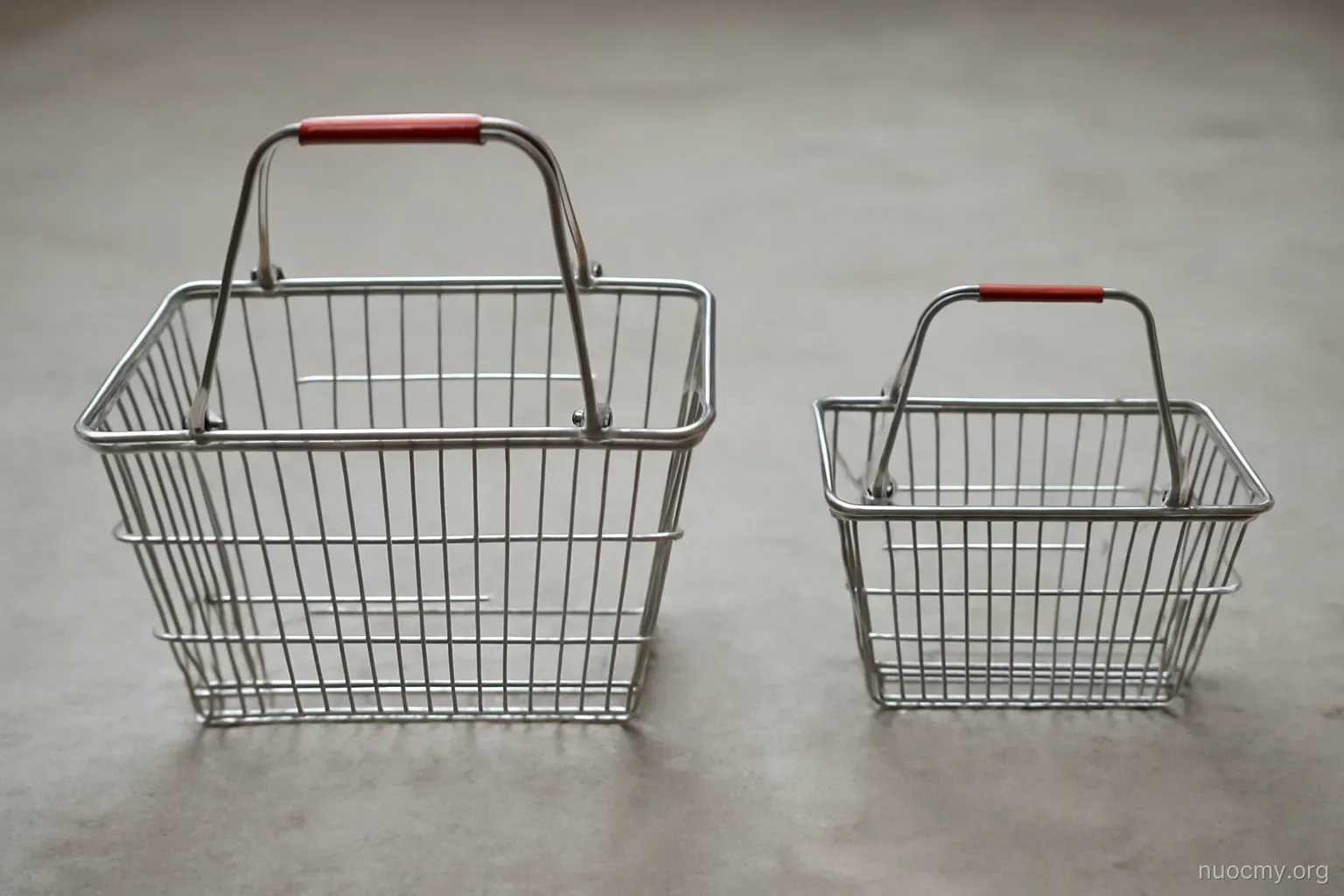two shopping baskets of different sizes placed side by side on a bare concrete floor