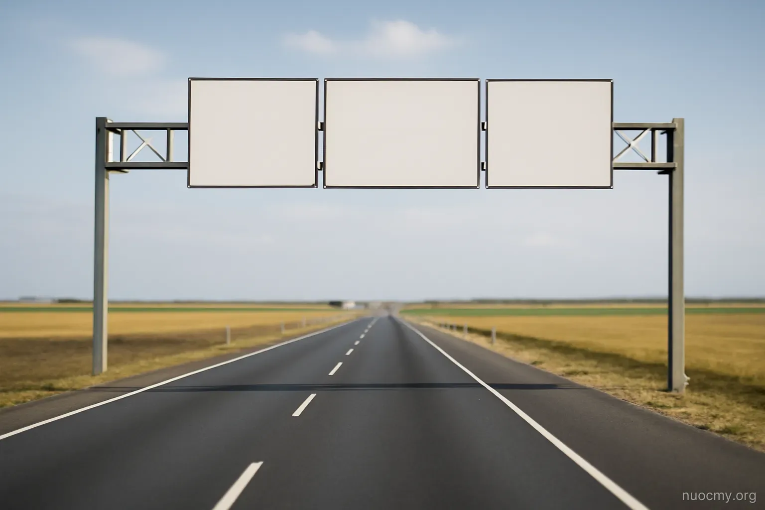a road sign gantry over an empty highway at a border between two flat farmland areas