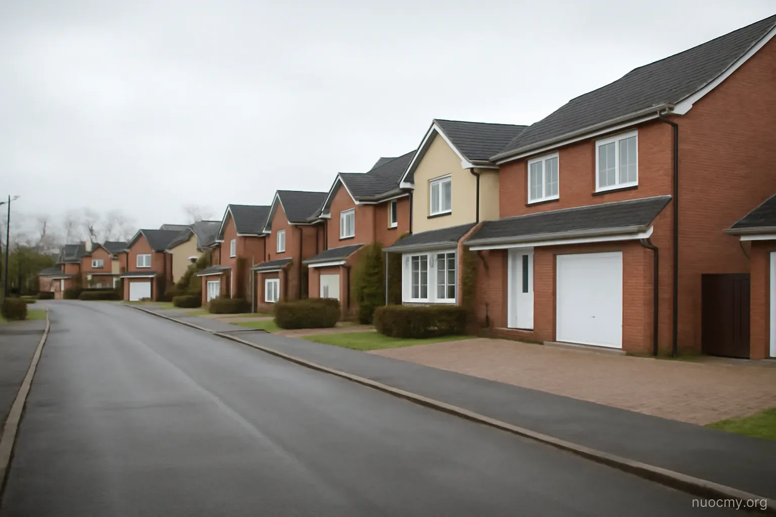 a suburban street of detached houses with wide driveways and no pedestrians, overcast afternoon