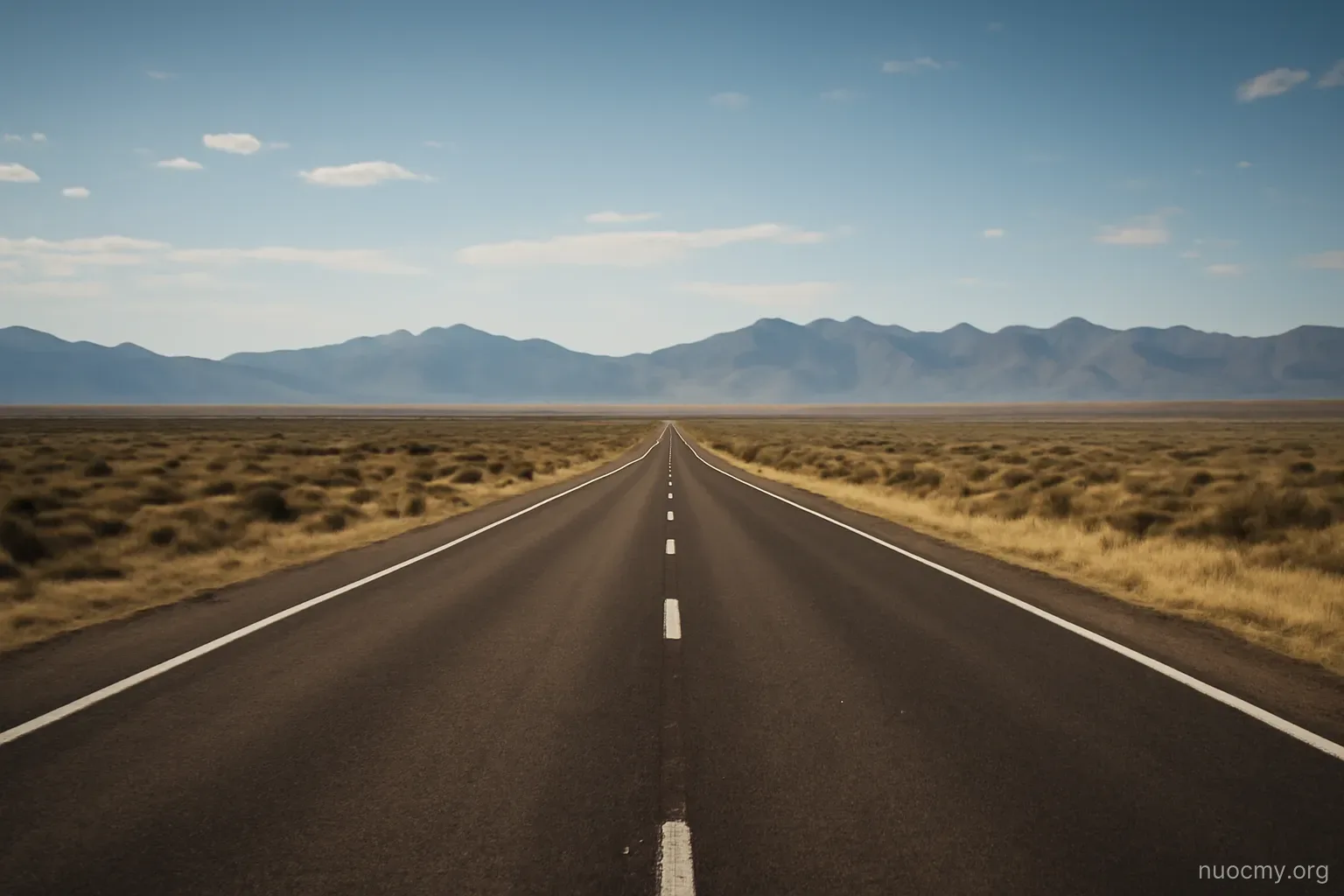a wide highway stretching toward distant mountains under an open sky with no buildings in sight