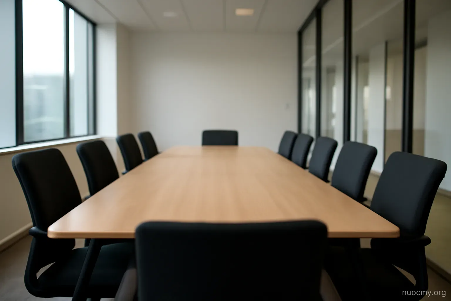 an empty meeting room with a long table and chairs pushed in, glass wall facing a corridor