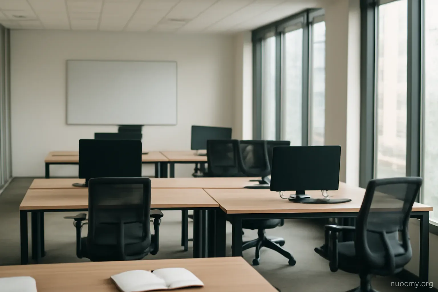 an open plan office with empty desks, a whiteboard wiped clean, and daylight from tall windows