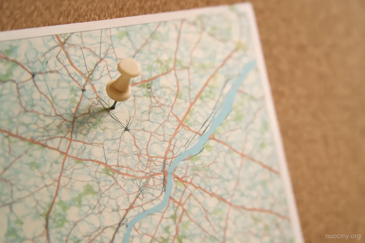 a map pinned to a corkboard with one pin placed near a small cross symbol drawn on it